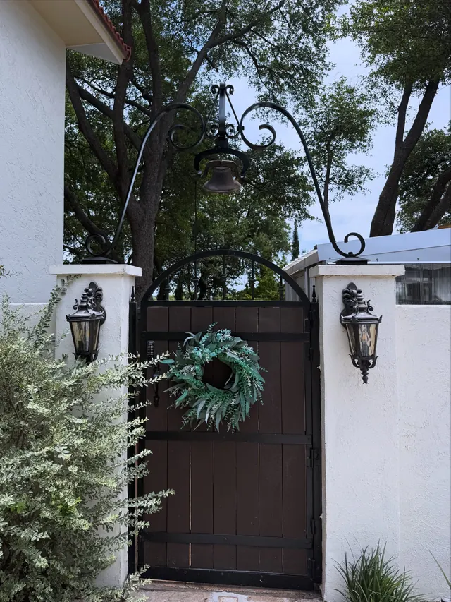 A steel arch over a courtyard gate between two white pillars, with scrolled lantern hangers and wall lanterns either side