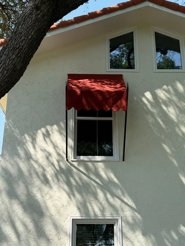 A refurbished red awning over a window on a stucco wall under a tree