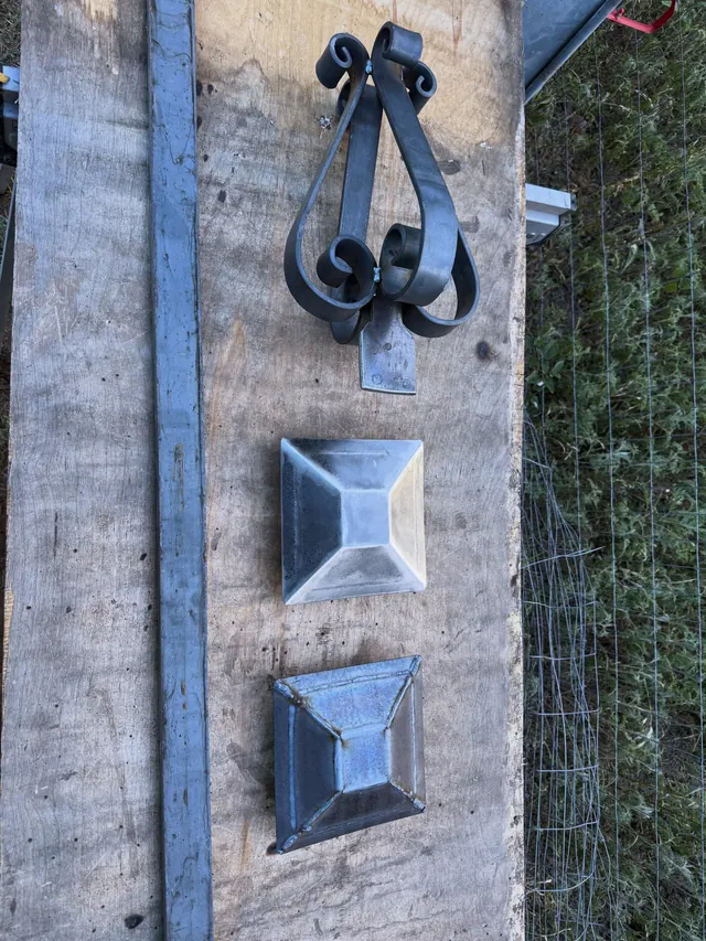 A scrolled bracket and two pyramid post caps set out on a timber plank