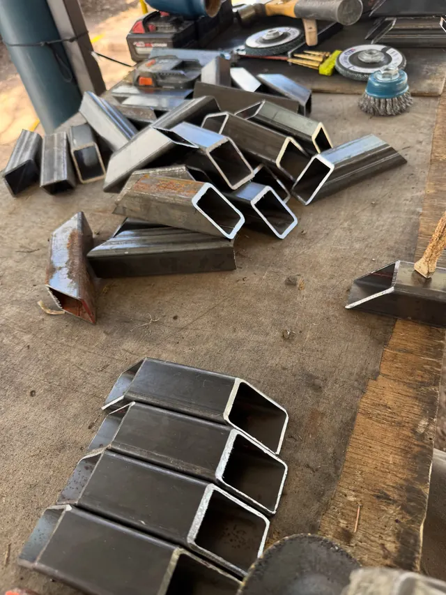 A pile of square steel tube cut to length with angled ends on the workshop floor