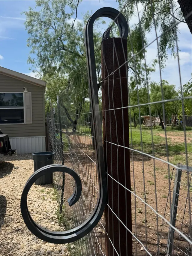 A tall black scrolled steel post finial curling off a timber fence post in a yard