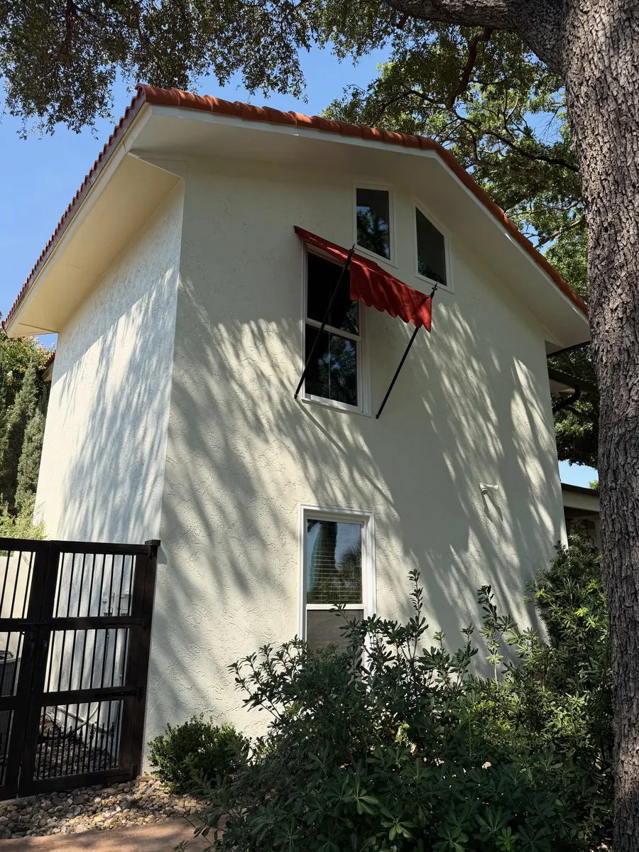 The side of a two-storey stucco house with red awnings over the windows, the old frames refurbished and a new one matched in