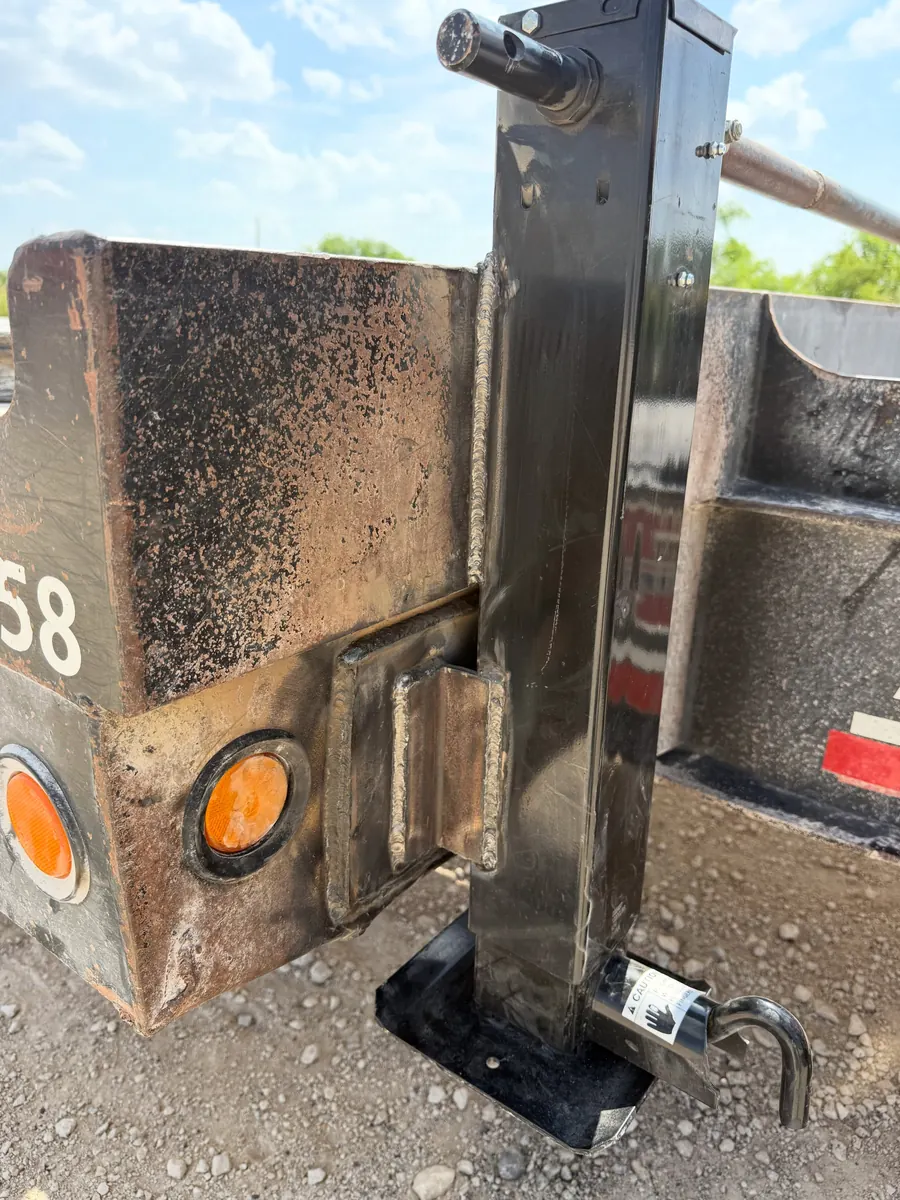 A replacement drop-leg jack welded onto the corner of a trailer frame, the fresh weld and new foot plate against the old dusty paint