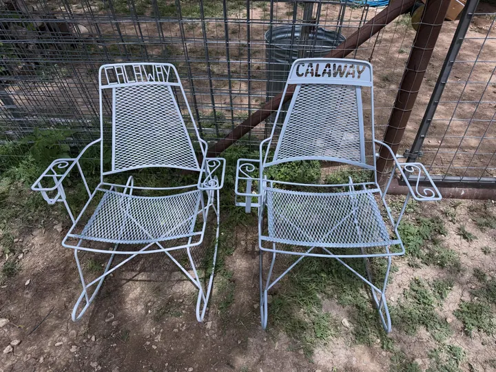 Two matching white wire-mesh patio rocking chairs side by side on the grass, one repaired and one built to match