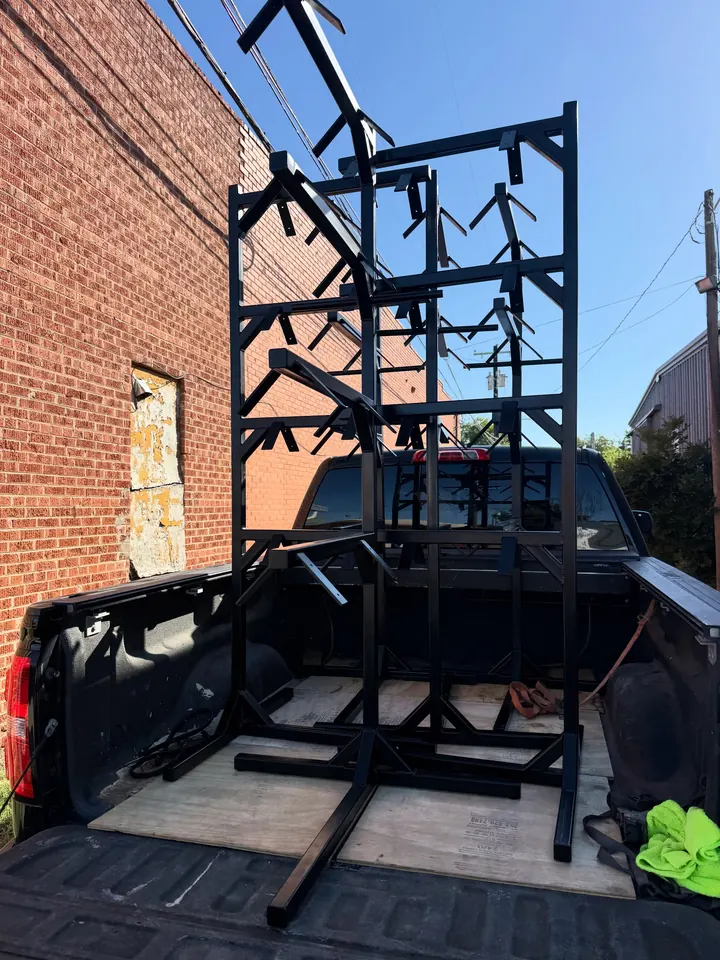 Six black steel saddle racks stacked upright in the bed of a pickup, ready for delivery