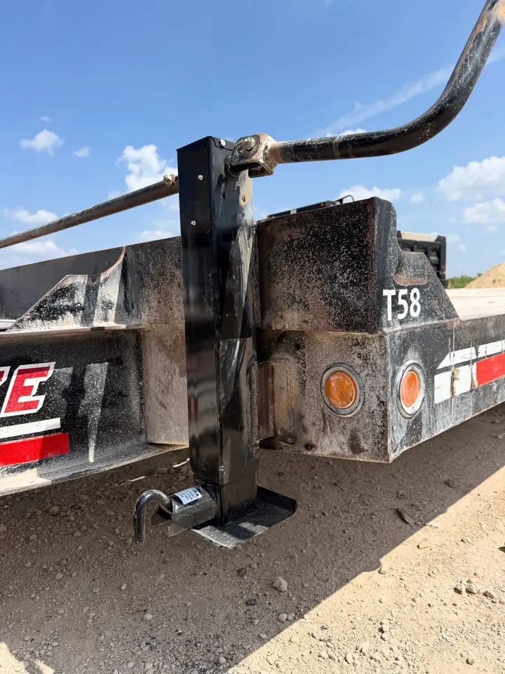 A new square-tube jack welded onto the corner of a black Interstate equipment trailer, standing on its foot plate in the dirt