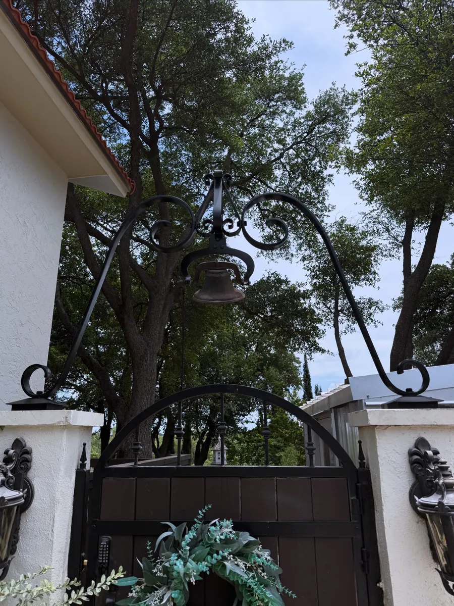 Looking up at the finished steel gate arch with its scrolled lantern hangers against the trees